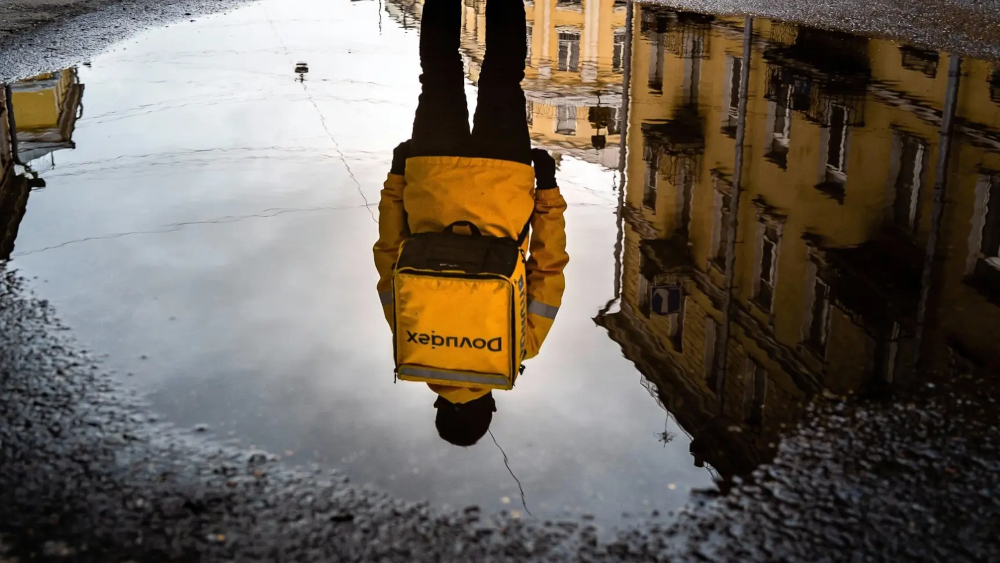 Курьер на электровелосипеде смотрит маршрут в телефоне на фоне городских улиц